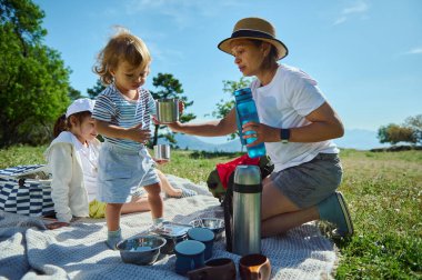 Bir anne ve çocukları güneşli bir pikniğin tadını çıkarıyorlar manzaranın ortasında, açık havada bağ kurmayı ve aile ilişkilerini huzurlu bir dağ ortamında kutluyorlar..