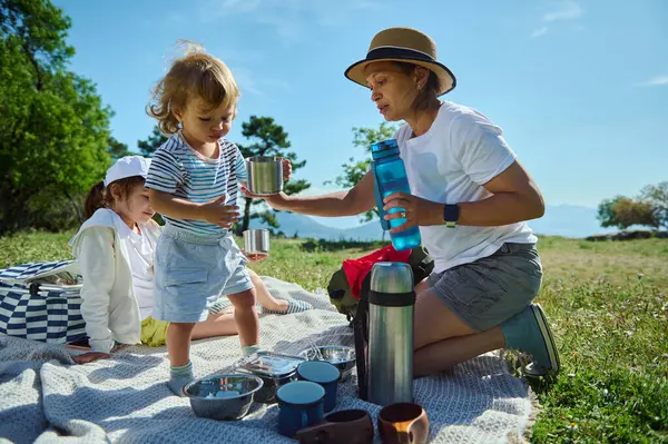 Bir anne ve çocukları güneşli bir pikniğin tadını çıkarıyorlar manzaranın ortasında, açık havada bağ kurmayı ve aile ilişkilerini huzurlu bir dağ ortamında kutluyorlar..