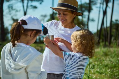 Bir anne, doğa pikniği sırasında çocuklarıyla dışarıda kaliteli zaman geçirir. Güneşin tadını çıkarır ve manzaralı dağ manzarası arasında bağ kurar..