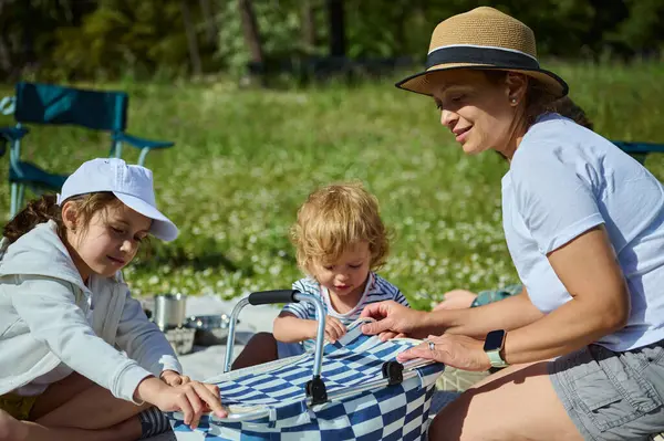 Neşeli bir aile pikniği bir anne ve çocukları, güneşli bir doğal ortamda açık hava aktiviteleri, güçlü aile bağlarını teşvik etmek ve mutlu yaz anıları yaratmak.