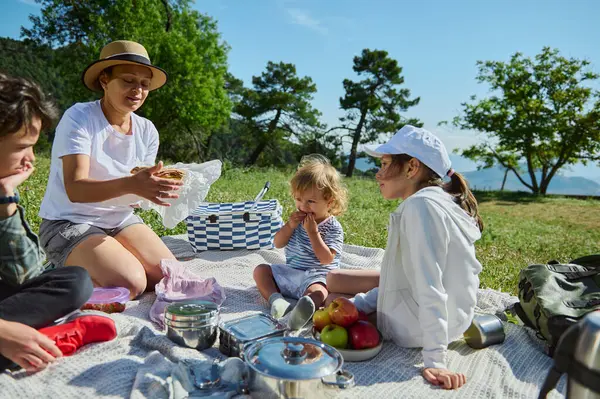Bir aile, dağ manzarasında keyifli bir piknik için toplanır. Doğanın ve güneşli havanın tadını çıkarırken aynı yemeği paylaşırlar. Rahatlamayı, bağlanmayı ve neşeyi yansıtırlar..