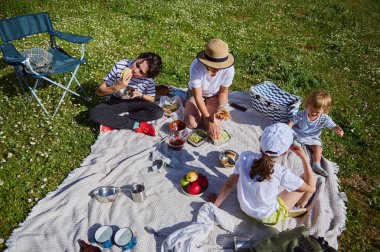 Bir aile açık havada çocuklarıyla güneşli bir yaz gününde doğal bir ortamda öğle yemeğinin tadını çıkararak vakit geçirir..