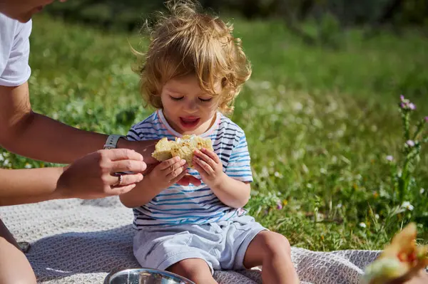Bir çocuk, güneşli bir piknik sırasında doğal ortamında annesiyle dışarıda kaliteli zaman geçirirken mısır yemekten hoşlanır..