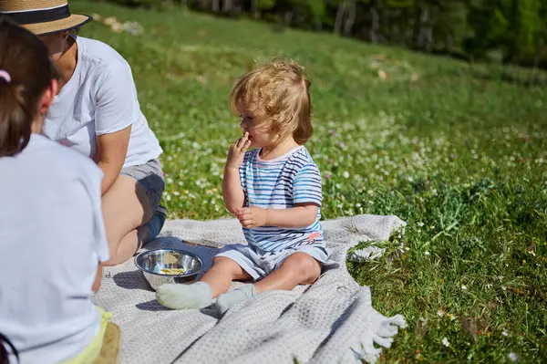 Bir anne ve çocukları güzel bir pikniğin tadını çıkarıyorlar. Etrafı resimli dağ manzaralarıyla çevrili, doğada birlikte geçirdikleri zamanı kutluyorlar..