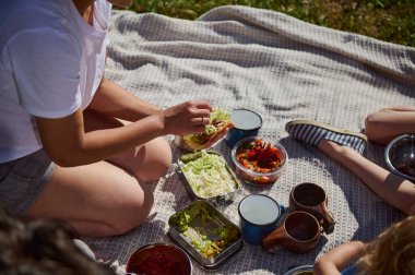 Güneşli bir günde aile pikniği hazırlamak ve ev yapımı tacoları paylaşmak, birliktelik, neşe ve doğal çevreyi vurgulamak..