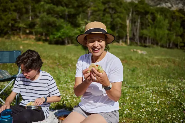 Bir aile, doğanın sakinliğiyle çevrili, güneşli açık gökyüzünün altında sıcaklığını, bağlantısını ve sağlıklı yaşam tarzını gösteren güzel bir çayırda açık hava yemeğinin tadını çıkarır..