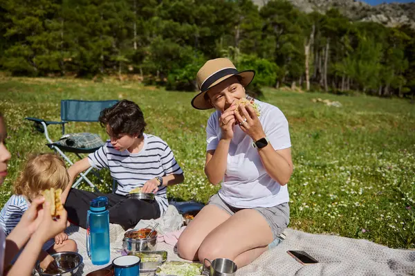 Neşeli bir anne dışarıda çocuklarıyla piknik yapar, sakin bir dağ çayırında tacoların tadını çıkarır. Beraberlik, eğlence ve bağlantı doğadaki bu sağlıklı, aktif anı karakterize eder..