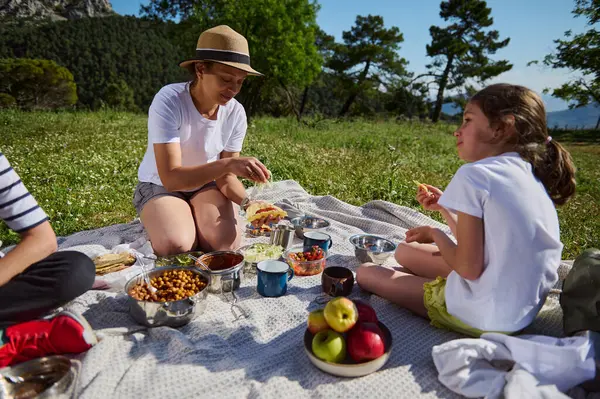 Aile güzel bir dağda piknik yapıyor, yiyecekleri paylaşıyor ve birlikte dışarıda vakit geçiriyorlar. Sahne neşe, bağlantı ve doğa ve sağlık için bir sevgi taşır..