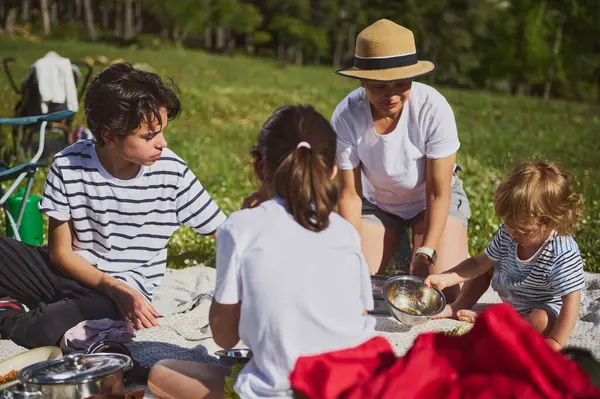 Aile, doğa ile çevrili bir piknikte dışarıda kaliteli zaman geçiriyor. Çocuklar huzurlu ortamın tadını çıkarırken yemek ve paylaşımla neşe içinde meşgul olurlar..