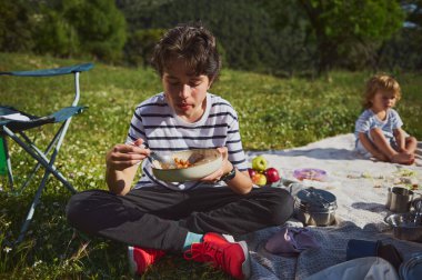 Aile üyeleri açık havada güzel bir dağ çayırında piknik yaparak güzel vakit geçirirler. Sahne beraberliği, rahatlığı ve doğanın güzelliğini yansıtıyor..