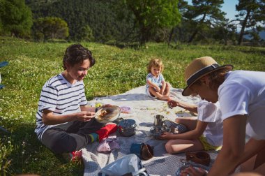 Neşeli bir aile, doğa tarafından çevrelenmiş güneşli ve aktif bir yaşam tarzının tadını çıkarırken dağlarda piknik yaparken birlik ve beraberlik sergiliyor..