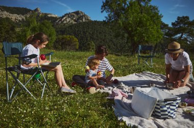 Neşeli bir aile, manzaralı dağ manzaralarının ortasında piknik yapar, kaliteli zaman ve yemekleri paylaşır ve doğayı takdir eder. Barışçıl bir ortamda birliktelik ve açık hava aktivitelerinin altını çiziyor.