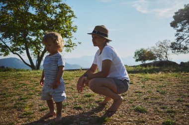 Bir anne ve yavrusu açık havada, ağaçlarla çevrili ve berrak bir gökyüzünün altında dağlık bir zemin altında huzurlu bir anın tadını çıkarıyorlar. Huzurlu atmosfer onların doğaya olan bağlılıklarını ve takdirlerini arttırır..