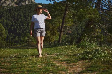 Yeşilliklerle çevrili canlı bir dağ manzarasında gezinen bir kadın. Sıcak güneş ışığı altında açık hava sükunetini seviyor, aktif ve sakin bir yaşam tarzını kucaklıyor..