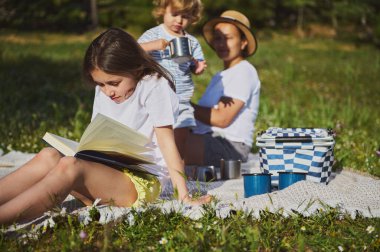 Huzurlu bir çim tarlasında birlikte zaman geçiren bir ailenin huzurlu bir görüntüsü. Güneş ışığı, açık hava pikniğinin sıcaklığını arttırıyor. Kaygısız ve neşeli bir anı vurguluyor..