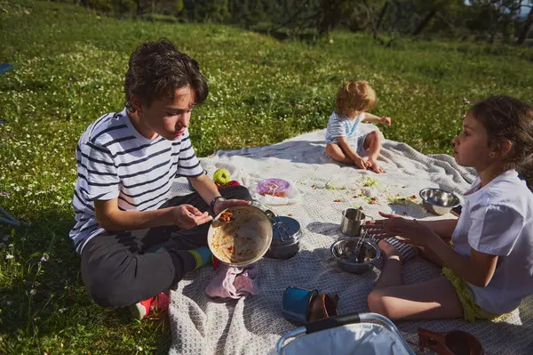 Neşeli bir aile güneşli bir günde pikniğin tadını çıkararak dışarıda birlikte kaliteli zaman geçirir. Çocuklar yemyeşil ortamda kahkaha ve yiyeceği paylaşıyor. Aktif ve sağlıklı bir yaşam tarzını kutluyorlar..