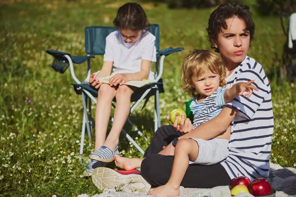 Doğayla çevrili güneşli bir açık hava pikniğinin tadını çıkaran bir aile. Sahne, bir birliktelik, keşif ve kırsal alanda kaynaşma hissi yakalıyor..