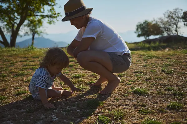 Bir anne, ağaçlarla çevrili çimenli bir arazide, doğadaki aile bağlarını ve keşiflerini ön plana çıkararak yavrusunun yanına çömelir..