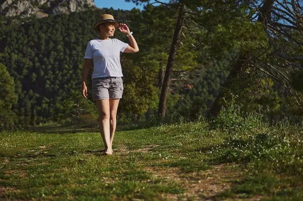 Yeşilliklerle çevrili canlı bir dağ manzarasında gezinen bir kadın. Sıcak güneş ışığı altında açık hava sükunetini seviyor, aktif ve sakin bir yaşam tarzını kucaklıyor..