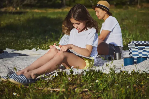 Açık havada bir aile anı, bir anne ve çocukları çevrenin yeşilliklerle çevrili olduğu bir pikniğin tadını çıkarırken, doğadaki beraberliğin huzuru ve neşesinin tadını çıkarırken..