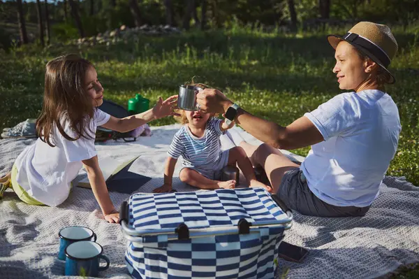 Bir anne ve iki çocuğunun piknik yaparken, doğal ortamdaki birlikteliği, sıcaklığı ve bağlantıyı sembolize ederken özel bir anı paylaştıkları sağlıklı bir sahne..