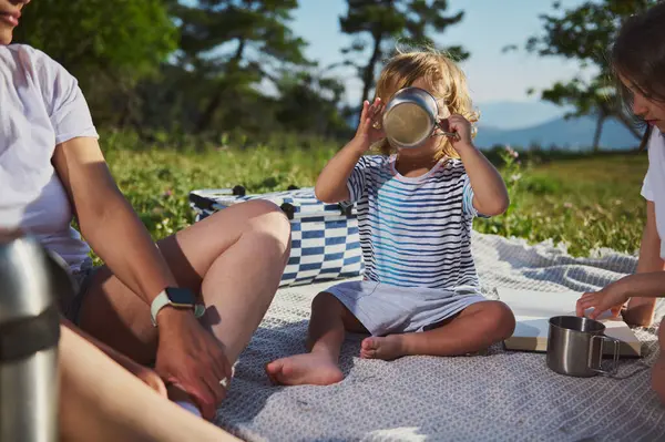 Bir anne ve çocukları güneşli bir günde dışarıda pikniğin tadını çıkarırlar. Etrafı güzel bir dağ manzarasıyla çevrilidir. Aile bağlarını, doğayı ve aktif bir yaşam tarzını teşvik ederler..