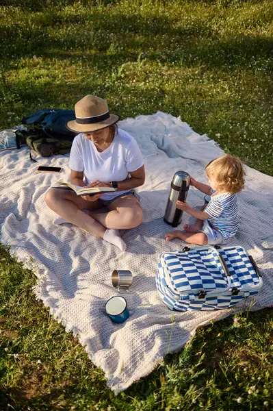 Bir annenin doğayla iç içe olan piknik aletleriyle uğraşırken kitap okuduğu huzurlu bir an. Sağlıklı bir yaşam tarzında aile birlikteliğini ve eğlenceyi teşvik ediyor..