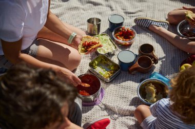 Ebeveynler ve çocuklar sakin bir açık hava pikniğinin tadını çıkarıyorlar, tacoları paylaşıyorlar ve doğayla iç içe geçiyorlar. Atmosfer aile bağlarını, sağlıklı beslenmeyi ve aktif bir yaşam tarzını yansıtıyor..