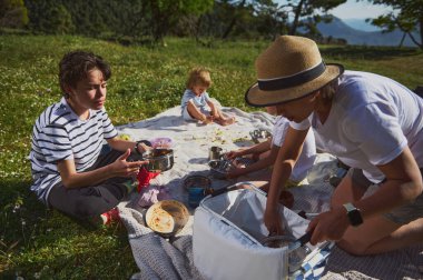 Neşeli bir aile piknik yemeğinin tadını çıkarıyor. Pahalı bir dağ ortamında, tahvilleri destekliyor ve açık havayı kucaklıyor. Doğal ortamda bir bağ ve rahatlama anı..