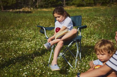 İki çocuk rahatlar ve kır çiçeği tarlasında güneşli bir günün tadını çıkarırlar. Kamp sandalyesinde oturup elma yerler. Resim boş zamanları, doğayı ve çocukluk anlarının basitliğini tasvir ediyor..