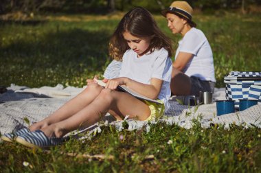 Açık havada bir aile anı, bir anne ve çocukları çevrenin yeşilliklerle çevrili olduğu bir pikniğin tadını çıkarırken, doğadaki beraberliğin huzuru ve neşesinin tadını çıkarırken..