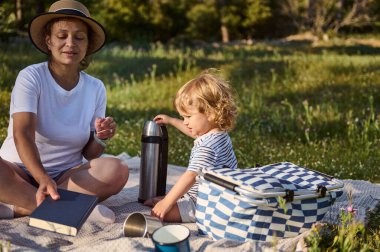 Bir anne ve çocuğun açık havada birbirine bağlandığı hoş bir piknik sahnesi. Arkaplan gibi pürüzsüz, doğal bir ortam. Aile aktivitelerini göstermek için biçilmiş kaftan..