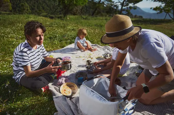 Neşeli bir aile piknik yemeğinin tadını çıkarıyor. Pahalı bir dağ ortamında, tahvilleri destekliyor ve açık havayı kucaklıyor. Doğal ortamda bir bağ ve rahatlama anı..