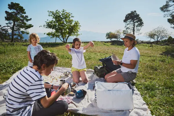 Bir aile açık hava pikniğinin tadını çıkarıyor. Manzaralı dağların ortasında. Güneşin altında neşeli bir anı paylaşıyorlar. Birlikte olmak ve eğlenmek için, bu görüntü sağlıklı açık hava aktivitelerini yakalar..