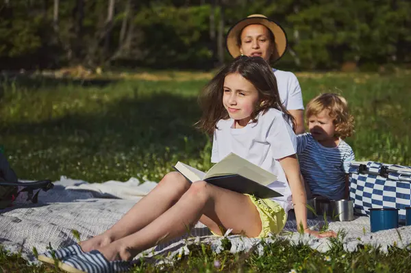 Bir anne ve çocukları dışarıda huzurlu bir pikniğin tadını çıkarıyorlar. Doğayla baş başa güzel vakit geçiriyorlar. Sıcak ve güneşli bir günde çocuklar yemyeşil ile çevrili iken rahatlar..
