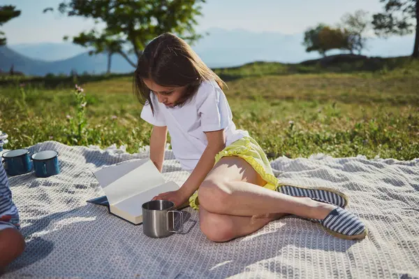 Mutlu bir çocuk yaz pikniği sırasında açık havada kitap okuyor. Doğayla iç içe, çarpıcı bir dağ ortamında, sıcak ve güneşli bir günün tadını çıkarıyor..