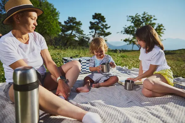 Doğanın güzelliği ile çevrili huzurlu bir pikniğin keyfini çıkaran neşeli bir aile sahnesi, ilişkileri, mutluluğu ve beraberliği açık hava ortamında vurguluyor..