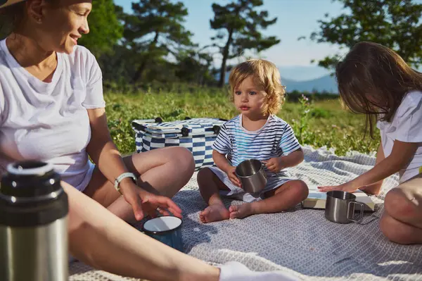 Neşeli bir anne, doğanın güzellikleriyle çevrili neşeli bir piknik sırasında ve dağlarda huzurlu bir günün tadını çıkarırken çocuklarıyla bir anı paylaşır..
