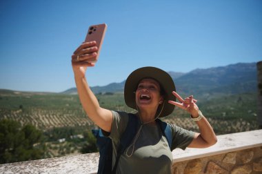 Bir gezgin, yuvarlanan yeşil tepelerin ve açık mavi gökyüzünün nefes kesici zeminine selfie çekerken sevinçle gülümser. Açık hava macerası ve doğal güzellik uyum içinde..