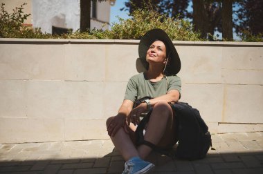 Açık havada sakin bir anın tadını çıkaran bir turist, parlak güneş ışığı altında oturur, keşif ve keşif yolculuğu sırasında doğayı ve rahatlamayı yansıtır..