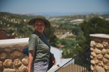 Sıradan kıyafetler giyen bir kadın büyüleyici bir tepe köyünün manzarasının tadını çıkarır. Arkaplan, geniş yeşil alanları ön plana çıkarıyor. Huzurlu ve davetkar bir atmosfer yaratıyor. Keşif için mükemmel..