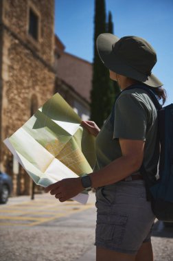 Elinde harita olan bir maceracı, tarihi bir ortaçağ köyünün sokaklarını keşfediyor. Günışığı, kültürel mirasın keşfini ve keşfini sembolize eden manzarayı vurguluyor.