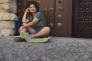 Bir gezgin, elinde haritayla eski bir dekoratif kapının yanında oturmuş tarihi mimarinin atmosferini seyrediyor. Sırt çantasıyla gelişigüzel giyinerek macera ve keşfin ruhunu yansıtıyorlar..