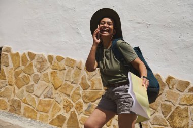 Neşeli bir gezgin, elinde bir haritayla güneşli tarihi bir köyde yürüyor ve bir sırt çantası taşıyor, macera ve neşeyi sembolize ediyor..