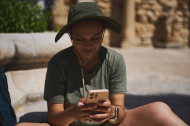 Bir gezgin, antik mimari ile modern teknolojiye zıt olarak, akıllı telefonuna dalmış, tarihi bir yerde duruyor. Güneşli sokaklar ve merak onun tarihteki yolculuğunu yeniden tanımlıyor..