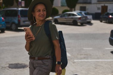 Bir gezgin dağlarla çevrili tarihi bir İspanyol köyünü keşfetmekten zevk alır, elinde akıllı bir telefonla. Açık hava kıyafetleri ve gülüşü keşfedilmenin sevincini manzaralı yerlerde aktarıyor..