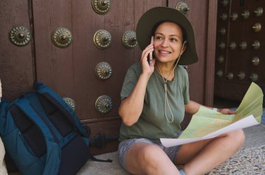 Gezgin, karmaşık bir şekilde tasarlanmış bir kapının yanında oturmuş, elinde bir harita, bir telefon kullanarak, ve maceralara hazır, tarihi yerlerdeki yolculuğun özünü yakalıyor..