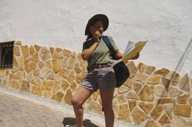 Hevesli bir gezgin, güneş ışığı altında tarihi bir taş köyü keşfederken bir harita incelerken macera ve merak ruhu sergiliyor..