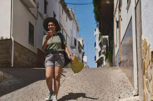 Maceracı elinde bir harita ve telefonla büyüleyici bir İspanyol kaldırım taşı caddesinde yürüyor, güneşli havayla geleneksel mimarinin tadını çıkarıyor..