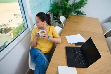 Rahatlamış bir kadın, modern bir çalışma alanında dizüstü bilgisayar ve belgelerle otururken, huzur ve verimliliği somutlaştırıyor..